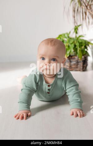 un bébé mignon à petites joues dans une combinaison verte est couché sur le sol à côté d'une maison. Photo de haute qualité Banque D'Images