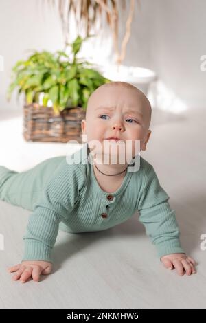 un bébé mignon à petites joues dans une combinaison verte est couché sur le sol à côté d'une maison. Photo de haute qualité Banque D'Images