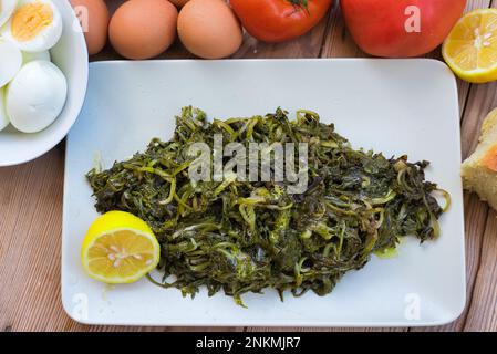 légumes verts sauvages bouillis, pissenlit, citrons et huile d'olive extra vierge, sur une table en bois. Horta ou Wild Greens. Cuisine grecque. Banque D'Images