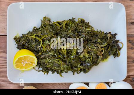 légumes verts sauvages bouillis, pissenlit, citrons et huile d'olive extra vierge, sur une table en bois. Horta ou Wild Greens. Cuisine grecque. Banque D'Images