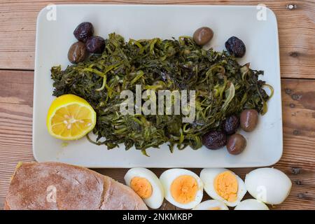 légumes verts sauvages bouillis, pissenlit, citrons et huile d'olive extra vierge, sur une table en bois. Horta ou Wild Greens. Cuisine grecque. Banque D'Images