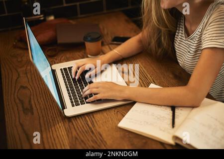 La technologie sans fil facilite la vie des étudiants. un jeune étudiant non identifiable utilisant son ordinateur portable pour étudier à une table de café. Banque D'Images