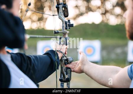 Archer mains, entraîneur et arc ou apprentissage de la flèche pour la compétition de tir à l'arc, défi de concentration d'athlète ou entraînement de fille. Enseignant, enseignant et homme Banque D'Images
