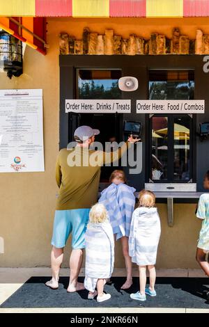 Père avec trois enfants commandant des rafraîchissements à la trappe de service Banque D'Images