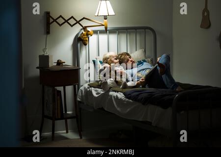 Grand frère lisant à la plus jeune sœur dans le lit avec la lampe allumée Banque D'Images