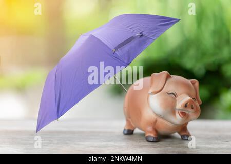 Tirelire et parapluie violet pour une protection sur un arrière-plan flou. Concept de finance et d'épargne. Banque D'Images