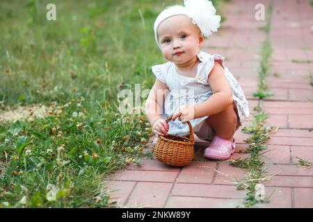 Une petite fille drôle dans une robe blanche s'assoit sur un chemin de dalle dans l'arrière-cour de la maison. Un enfant récolte des cerises à la ferme Banque D'Images