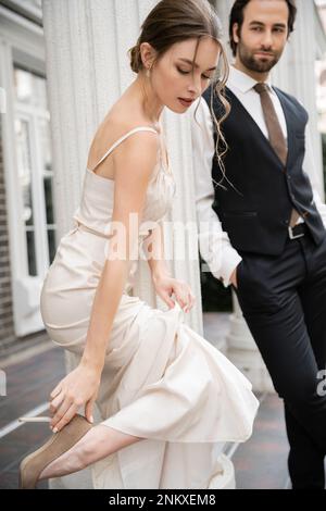 jolie mariée en robe de mariage portant une chaussure à talons hauts près du marié sur un arrière-plan flou, image de stock Banque D'Images