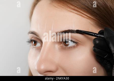 Esthéticienne appliquant la teinte pendant la procédure de correction des sourcils sur fond gris, gros plan Banque D'Images