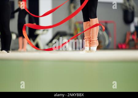 Image rognée des jambes de la petite fille, enfant, entraînement de gymnaste rythmique à l'intérieur, faire de l'exercice avec le ruban. Concept du sport, de l'enfance, du rythme Banque D'Images