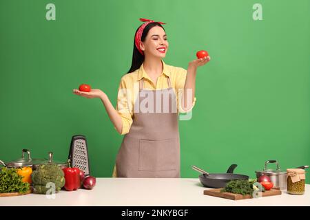 Jeune femme au foyer avec des légumes et différents ustensiles sur fond vert Banque D'Images