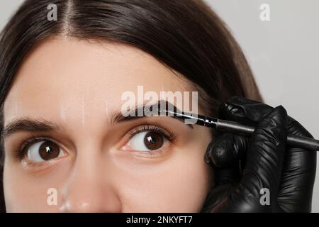 Esthéticienne appliquant la teinte pendant la procédure de correction des sourcils sur fond gris, gros plan Banque D'Images