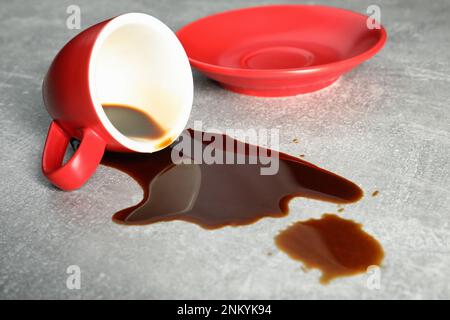 Tasse avec soucoupe et déversement de café sur table grise Banque D'Images