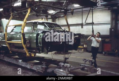 1970s Amérique : sur la chaîne de montage Cadillac --le câblage est complet sur cette carrosserie, et maintenant le travailleur le « va » à travers un trou dans le plancher à la chaîne de montage principale ca. 1973 Banque D'Images