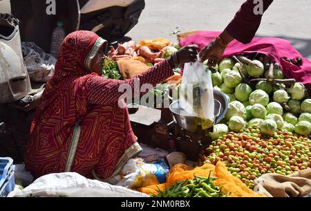 Une vendeuse de marché qui remet un sac de marchandises à un client alors qu'elle vend des fruits et des légumes de son magasin au bord du trottoir assis sur le sol Banque D'Images