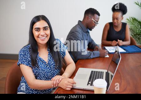Une femme d'affaires indienne s'assoit à la table de conférence avec ses collègues, à l'aide d'un ordinateur portable Banque D'Images