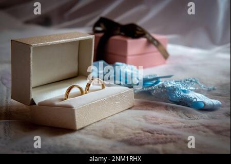 anneaux de mariage et détails une boîte blanche avec anneaux de mariage et une jarretière bleue couchée sur le lit sur fond de voile blanc Banque D'Images