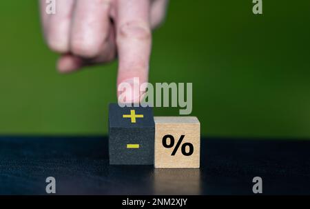 Symbole d'augmentation des taux d'intérêt. La main tourne un cube en bois et change l'expression 'pourcentage moins' en 'pourcentage plus'. Banque D'Images