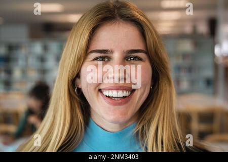 Une jeune fille heureuse souriant dans l'appareil photo tout en se tenant à l'intérieur de la bibliothèque universitaire Banque D'Images