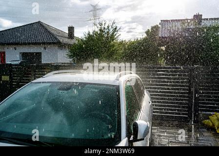 Une voiture de tourisme argentée garée dans l'allée devant le garage sous la pluie battante pendant un déversage. Banque D'Images