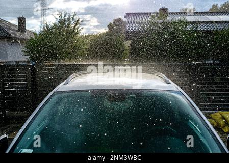 Une voiture de tourisme argentée garée dans l'allée devant le garage sous la pluie battante pendant un déversage. Banque D'Images