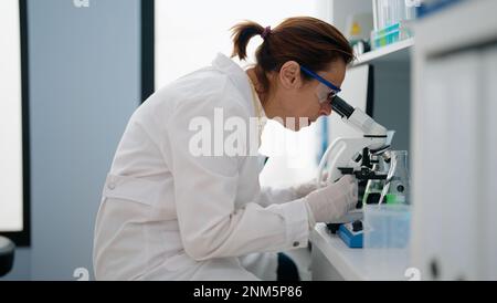 Femme hispanique d'âge moyen portant l'uniforme scientifique au microscope en laboratoire Banque D'Images