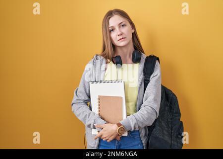 Jeune femme caucasienne portant le sac à dos d'étudiant et tenant des livres qui ont l'air endormi et fatigué, épuisé pour la fatigue et la gueule de bois, les yeux paresseux dans la mornin Banque D'Images
