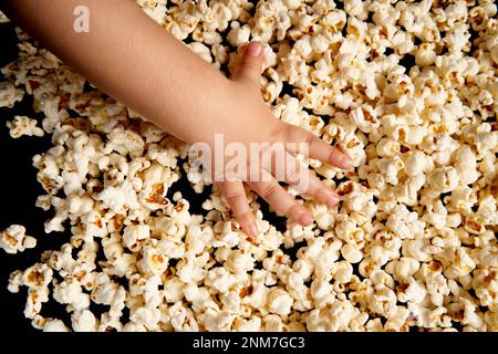 Les mains des enfants ramasseurs le pop-corn. Flat lay . Le concept d'anniversaire, de fête, de vacances, de loisirs à la maison. Copiez l'espace pour votre produit. Texture ou arrière-plan du pop-corn. Banque D'Images