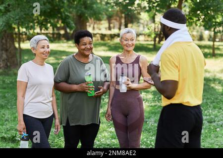 Groupe diversifié de femmes âgées qui s'entraînent dans des sports de plein air et qui parlent à l'entraîneur Banque D'Images