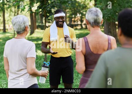Portrait d'un entraîneur souriant parlant à divers groupes de femmes âgées pendant l'entraînement sportif en plein air Banque D'Images