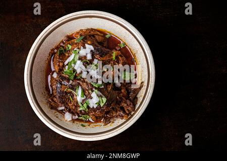 Un bol de viande de birria lentement cuite et braisée dans un bol vintage sur fond marron foncé avec espace de copie Banque D'Images