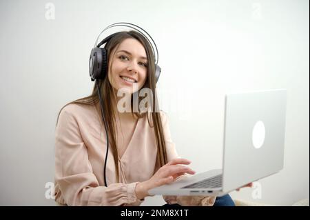 Engagé dans l'entraînement à distance. Une jeune femme active travaillant à distance participe à une réunion virtuelle à l'aide d'un ordinateur à domicile. Une étudiante participe à une visioconférence en portant un casque. Photo de haute qualité Banque D'Images