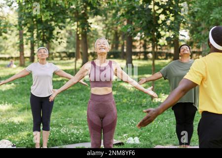 Groupe de femmes âgées actives qui profitent du yoga à l'extérieur du parc et font des exercices de respiration Banque D'Images