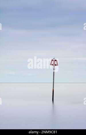 Un marqueur d'aine rouge de défense de plage au milieu d'une mer et d'un ciel parfaitement calmes (portrait) Banque D'Images