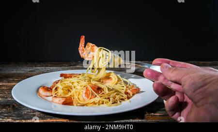 Spaghetti aux crevettes sur la fourchette dans les mans avait avec fond noir et l'espace de copie Banque D'Images