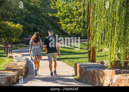 Petit ami en short et petite amie en robe stoll vers le bas curving sentier de parc public près de grands rochers et saule arbre sur joli da été Banque D'Images