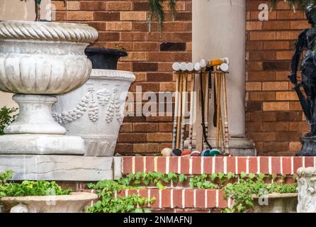 Le croquet se penche contre un pilier, entre des pots de fleurs et des statues et des plantes sur le porche d'une maison haut de gamme - gros plan Banque D'Images