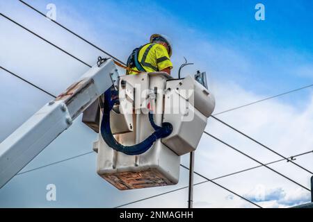 Ouvrier électricien en gilet de sécurité vert et casque en pont roulant travaillant sur des lignes hautes ou des feux de circulation en plein air avec fond de ciel Banque D'Images