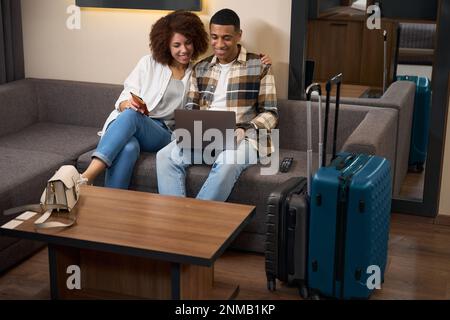 Homme et femme souriants sont assis sur un canapé avec ordinateur portable Banque D'Images