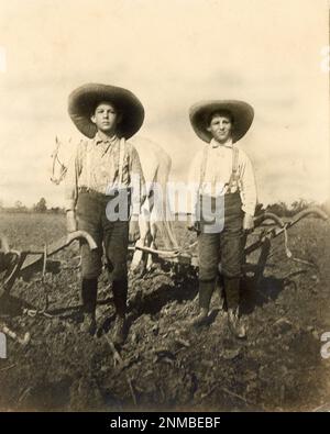Farm Boys début 1900, labourage de champs avec des charrues en bois, enfants de ferme d'époque, champ de ferme, charrue tirée par des chevaux, vie de ferme du début du siècle Banque D'Images