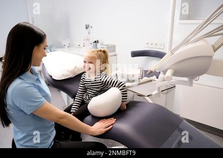 La première fois qu'une fille à la réunion de dentiste conversation fille s'assoit exactement dans la chaise regarde le médecin elle a peur de la dernière technologie redresser dos rayé blouse doux jouet dents blesser Ukraine 2023 Banque D'Images