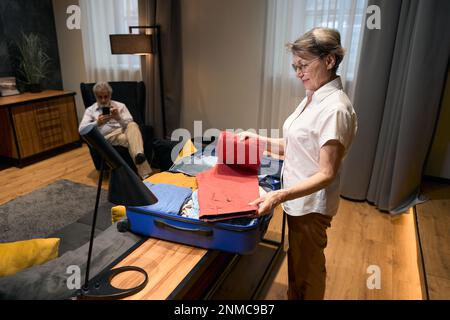 Une vieille femme aidant son mari à plier ses vêtements dans un sac à roulettes Banque D'Images
