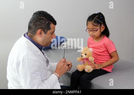 Le médecin pédiatre Latino vérifie sa jeune patiente avec le trouble du spectre de l'autisme ASD, il communique par l'intermédiaire de son ours en peluche Banque D'Images