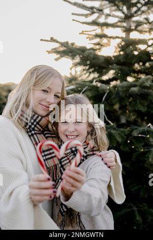 Deux filles avec des coeurs de canne en sucre devant un arbre de Noël Banque D'Images