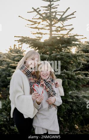 Deux filles avec des coeurs de canne en sucre devant un arbre de Noël Banque D'Images