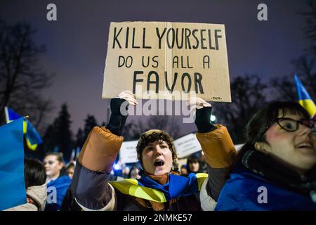 Un manifestant drapé par le drapeau ukrainien scanne des slogans et tient une pancarte exprimant son opinion lors de la manifestation anti-guerre de Varsovie. Des milliers de Polonais, d'Ukrainiens et de Biélorusses se sont réunis à l'extérieur de l'ambassade de Russie à Varsovie pour protester contre l'agression russe contre l'Ukraine et pour manifester leur solidarité avec l'Ukraine, à l'occasion de l'anniversaire de l'agression.les manifestants détenaient leurs drapeaux nationaux et affichaient également les noms écrits des Ukrainiens tombés dans la guerre. La foule s'est ensuite rendue au Parlement pour faire pression en faveur d'un soutien continu à l'Ukraine et de la condamnation de la guerre. Banque D'Images