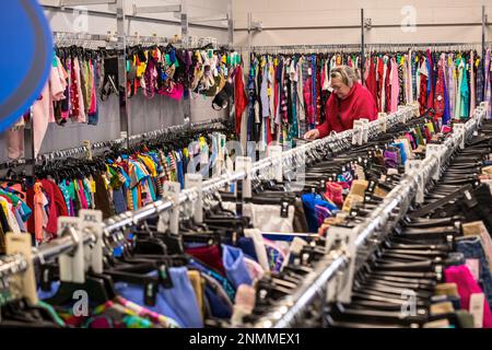 Femme âgée en blouson rouge traversant les porte-vêtements usagés à une rive thrift (bonne volonté) à Ludington, MI, États-Unis. Banque D'Images