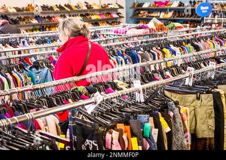 Femme âgée en blouson rouge traversant les porte-vêtements usagés à une rive thrift (bonne volonté) à Ludington, MI, États-Unis. Banque D'Images