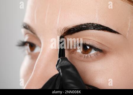 Esthéticienne appliquant la teinte pendant la procédure de correction des sourcils sur fond gris, gros plan Banque D'Images