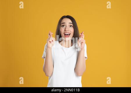 Jeune femme excitée tenant les doigts croisés sur fond jaune. Superstition pour bonne chance Banque D'Images